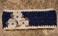 Handmade crocheted headband in navy blue with silver sparkle, a ruffled white edge, and a cluster of white flowers with blue bead centers