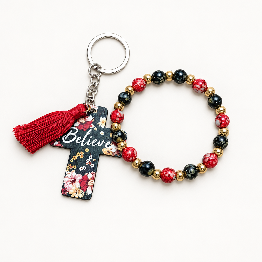 Red, black, and gold beaded stretch bracelet with silver cross charm beside a black cross tag keychain with red florals, Believe lettering, and red tassel