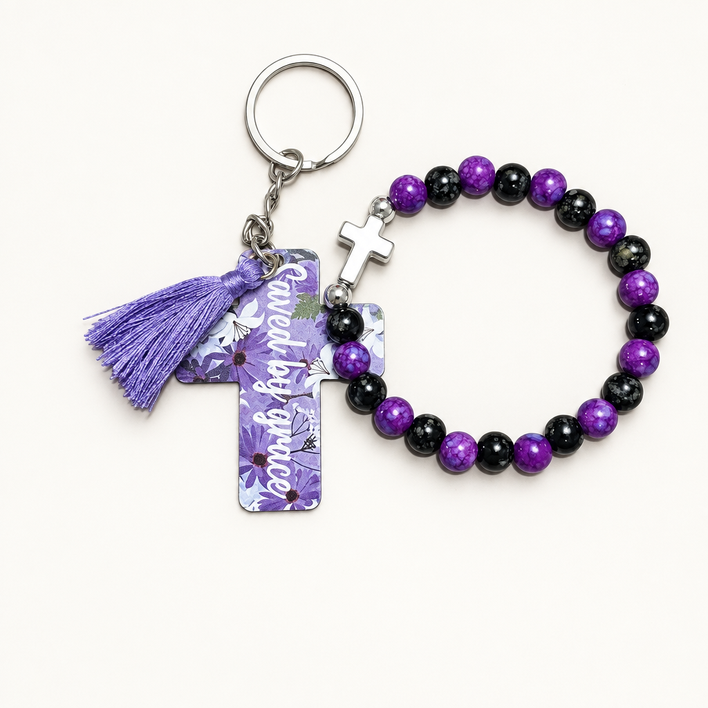 Royal purple and black beaded stretch bracelet with silver cross charm beside a lavender cross tag keychain with purple florals, saved by grace lettering, and purple tassel
