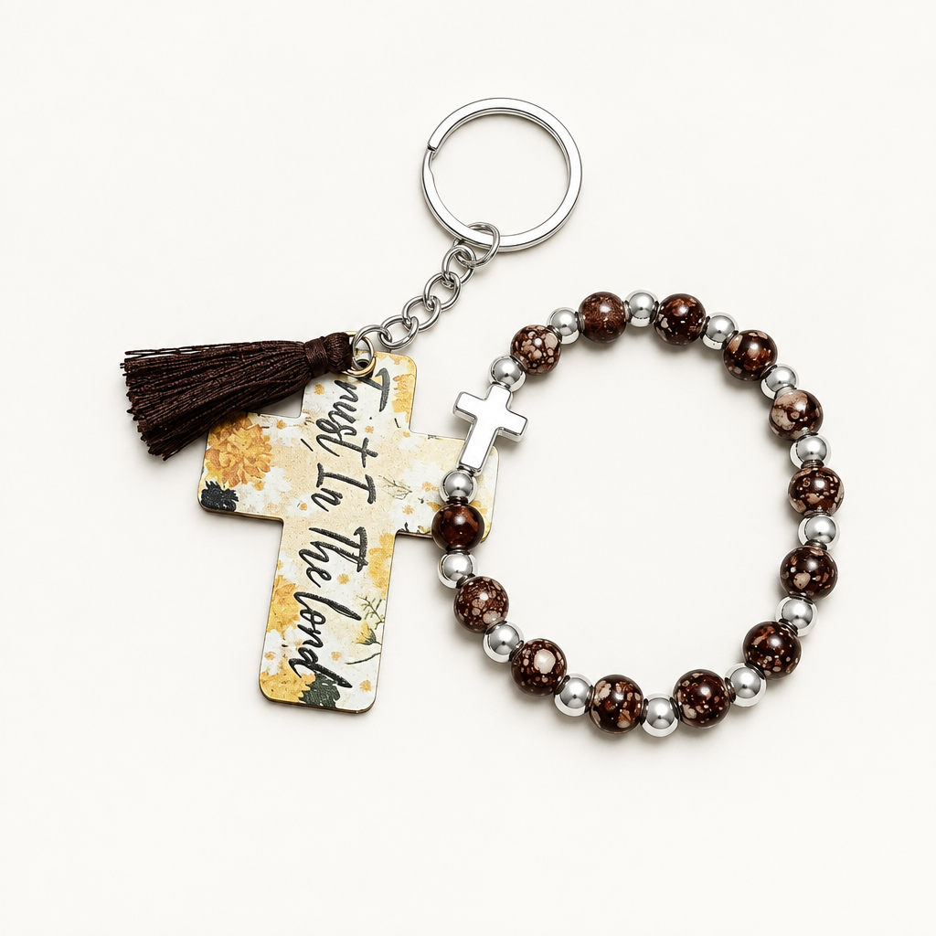 Chocolate brown beaded stretch bracelet with silver cross charm beside a cream cross tag keychain with warm florals, Trust In The Lord lettering, and brown tassel